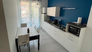 Una cucina moderna con mobili bianchi, un tavolo da pranzo con sedie, una parete di colore blu e una finestra con tende leggere.