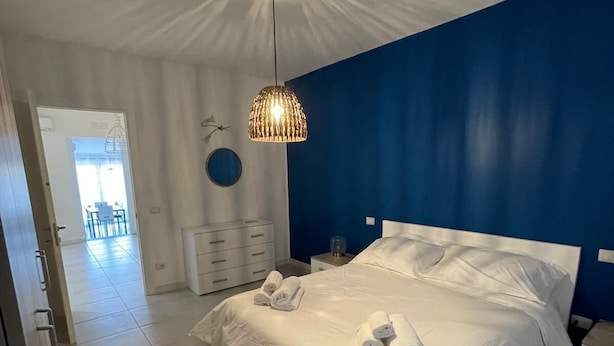Camera da letto con un grande letto, biancheria da letto bianca, una lampada a sospensione e vista sulla stanza adiacente.