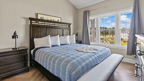 Een slaapkamer met een groot bed, een houten hoofdbord, een nachtkastje, een dressoir en een raam met uitzicht.