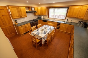 A compact kitchen with wooden cabinets, a dining table set for four, and a window providing natural light. - Kotirana near Fort William (Banavie)