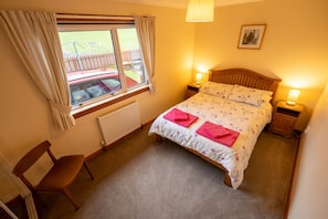 A bedroom with a bed, two bedside lamps, a chair, a window with curtains, a radiator, and a picture on the wall. - Kotirana near Fort William (Banavie)