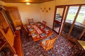 A dining area with a wooden table set for four, surrounded by chairs, a patterned carpet, and a view through a glass door. - Kotirana near Fort William (Banavie)