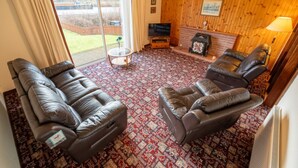 Un salon avec deux canapés en cuir, un téléviseur, une cheminée et un tapis à motifs.