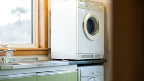 Un espace buanderie compact comprenant un lave-linge à chargement frontal et un sèche-linge, une fenêtre donnant sur les arbres et un meuble en bois.