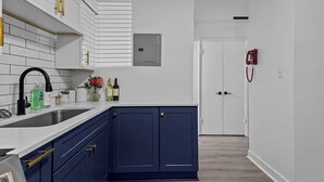 Eine moderne Küche mit weißen und blauen Schränken, einer Edelstahlspüle und einem roten Rauchmelder an der Wand.