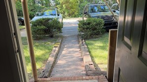 Eine Fußmatte am Eingang eines Hauses, ein Weg führt zu den geparkten Autos.