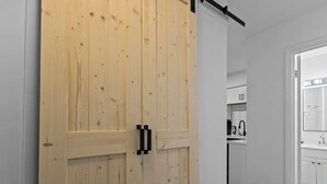 Eine Holztür, die zu einer Küche mit weißen Schränken und einer schwarzen Arbeitsplatte führt.
