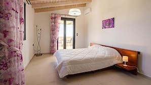 A bedroom with a wooden headboard, a bed with a white quilt, a bedside lamp, and a door leading to a balcony. - Alkistis Villa with amazing sea view (Rethymno)