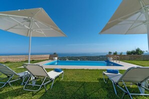 Zona de piscina con dos sombrillas, dos sillas de descanso y vista al océano.