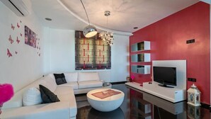A modern living room with a white sofa, a round coffee table, a flat-screen TV on a white stand, and a red accent wall. - Alkistis Villa with amazing sea view (Rethymno)