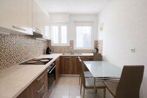 A modern kitchen with a dining area, featuring a large island, built-in oven, and a window providing natural light. - Athens Retreat - 2BD Apt Near Transport by MPS (Athina)