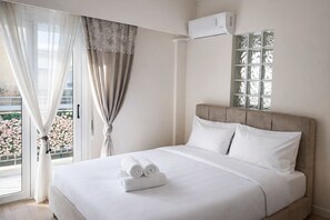 A hotel room with a bed, white linens, a window with patterned curtains, and an air conditioning unit. - Athens Retreat - 2BD Apt Near Transport by MPS (Athina)