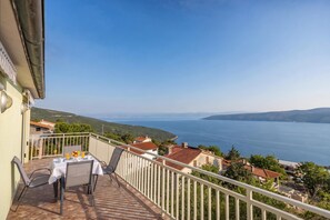 A balcony with a table set for two, overlooking a coastal landscape. - Sea View Apartments Magda (Krsan)