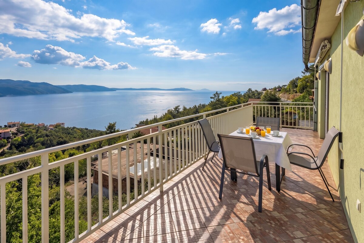 A balcony with a table set for breakfast overlooking a body of water and distant hills.