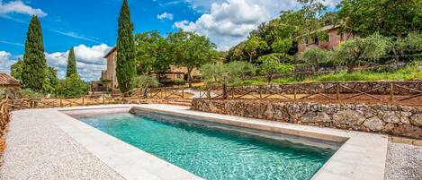 A rectangular pool with clear water, surrounded by a stone wall and a wooden fence.