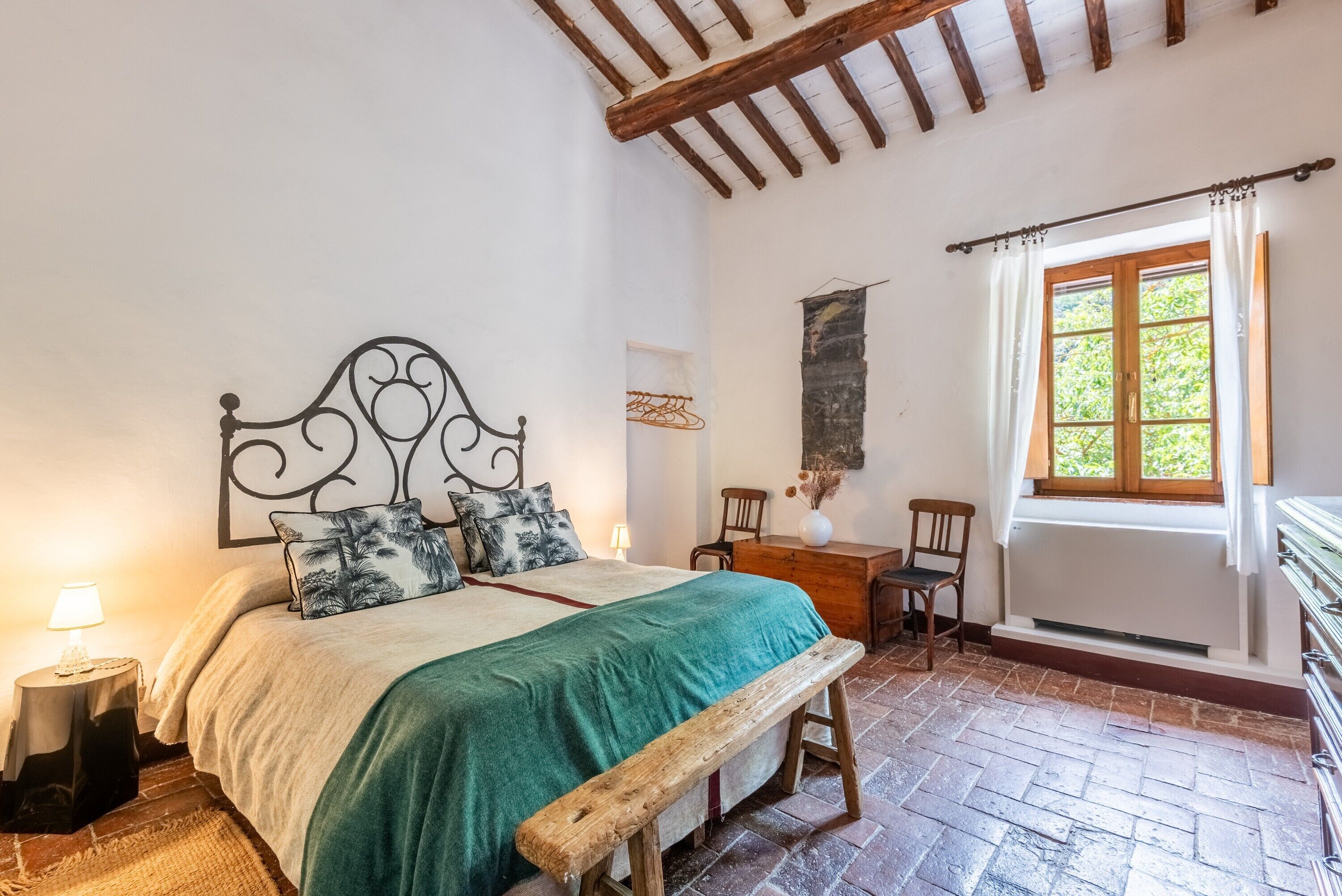 A bedroom with a bed, wooden bench, and a window with curtains.