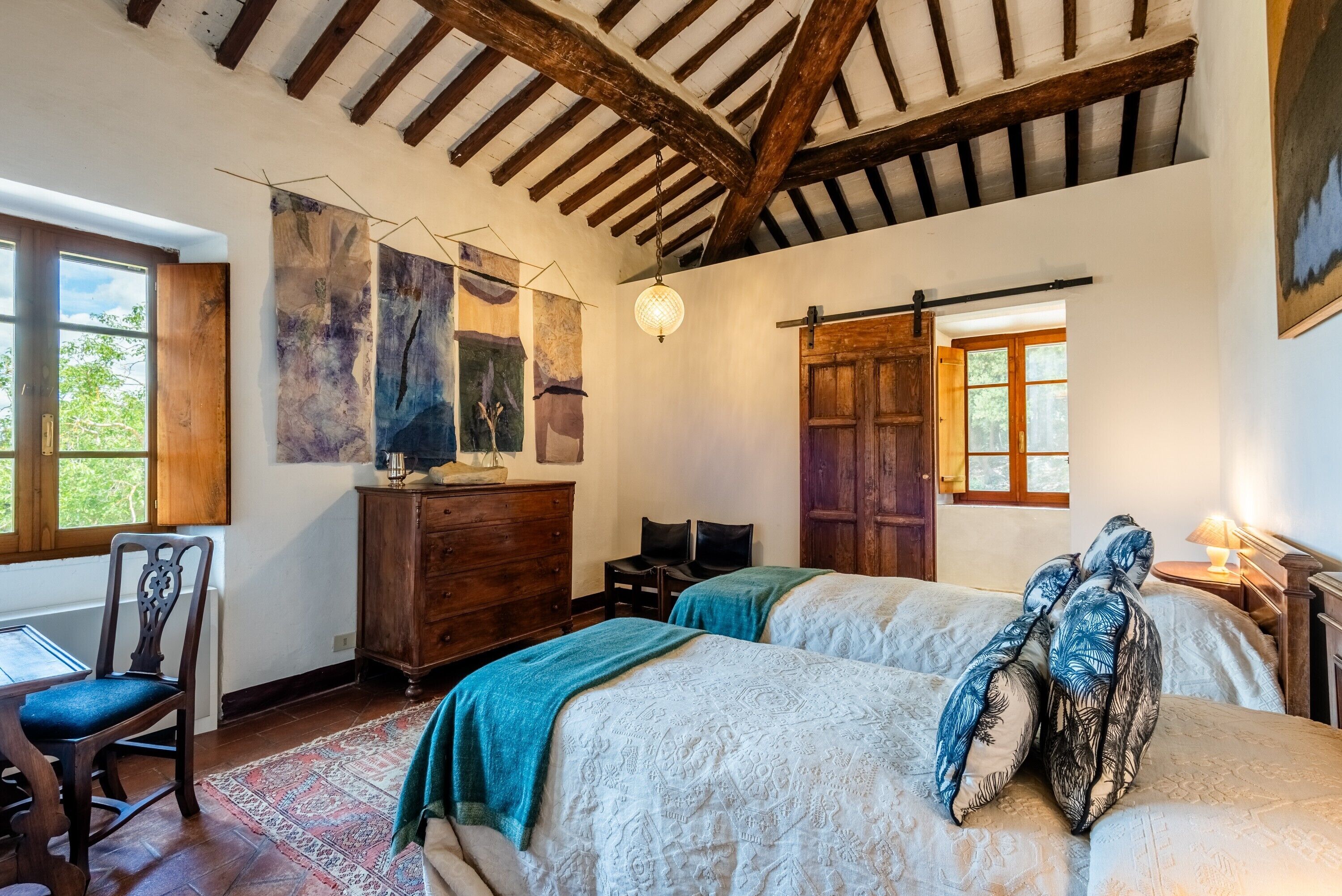 A room with two beds, a wooden dresser, a desk with a chair, and a large abstract painting on the wall.