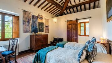 A room with two beds, a wooden dresser, a desk with a chair, and a large abstract painting on the wall.