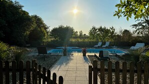 En swimmingpool med liggestole, omgivet af et træhegn og træer.