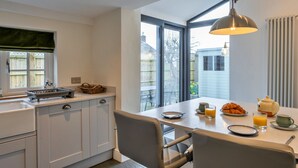 Een moderne keuken met een eethoek, voorzien van een groot raam, een hangende hanglamp en ontbijtartikelen op tafel.