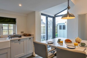 Eine moderne Küche mit Essbereich, ausgestattet mit einem großen Fenster, einer hängenden Pendelleuchte und Frühstücksangeboten auf dem Tisch.