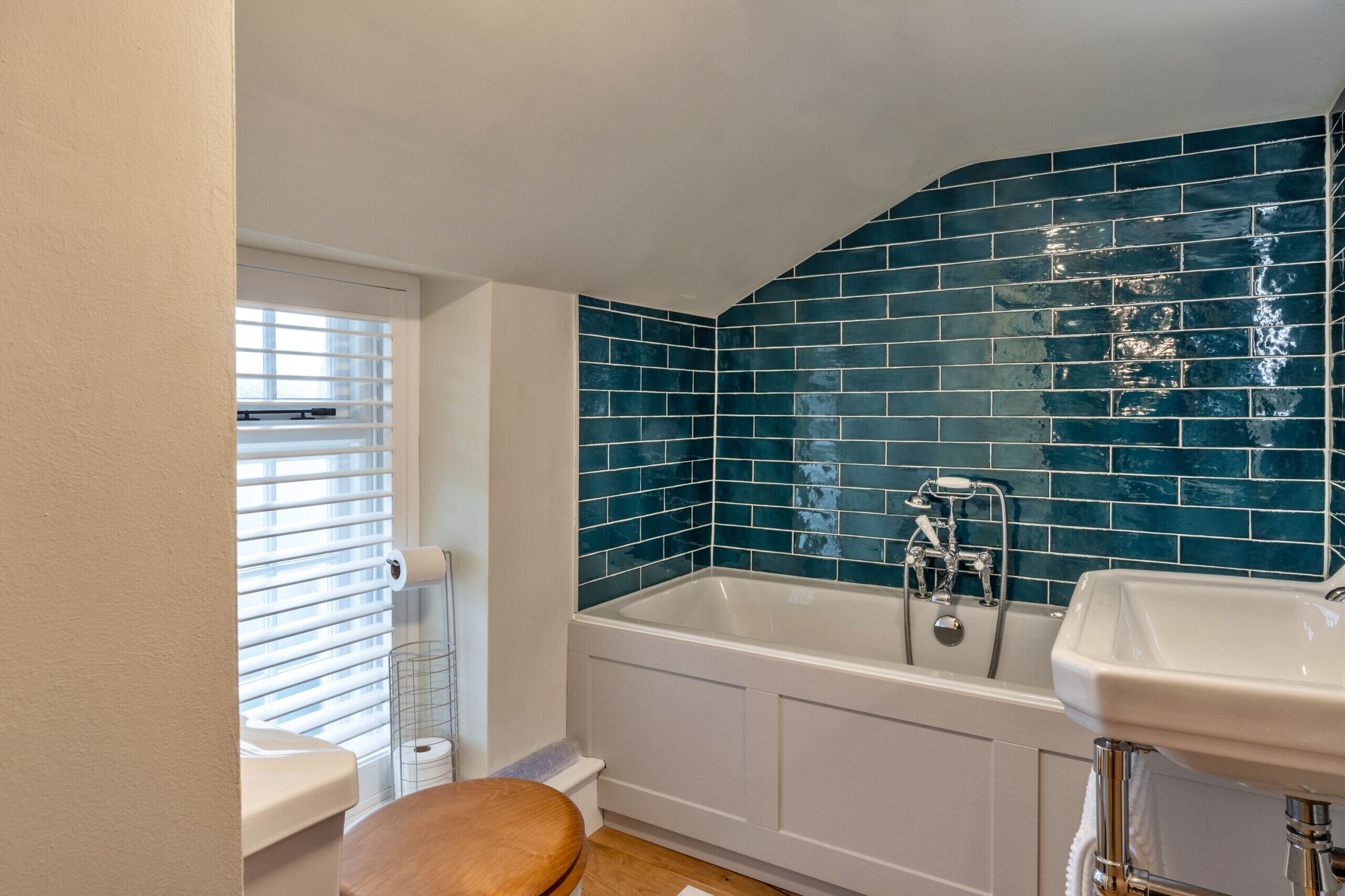 A bathroom with a white bathtub, a white sink, and a wooden toilet seat.