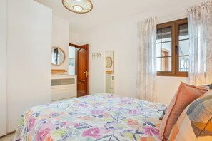 Une chambre à coucher avec un lit, une commode, un miroir, une fenêtre avec des rideaux et une porte.