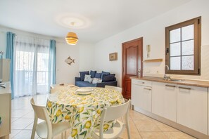 Une cuisine moderne avec des meubles blancs, une table à manger recouverte d’une nappe à motifs citronniers et un canapé bleu dans l’espace salon.