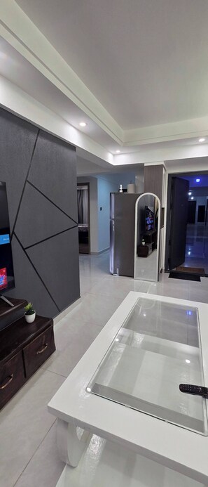 Una sala de estar moderna con una mesa de centro de vidrio, un televisor de pantalla plana y un mueble bajo de madera oscura.