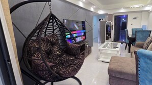 A modern living room with a hanging chair, a sofa, a coffee table, and a TV. - Brand New Westlands 2BR 2Ba Walk to Sarit GTC (Nairobi)