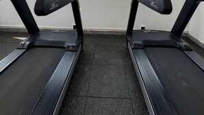 Two treadmills with digital displays, a tiled floor, and a view of a construction site through large windows. - Brand New Westlands 1BR 1Ba Walk to Sarit GTC (Nairobi)