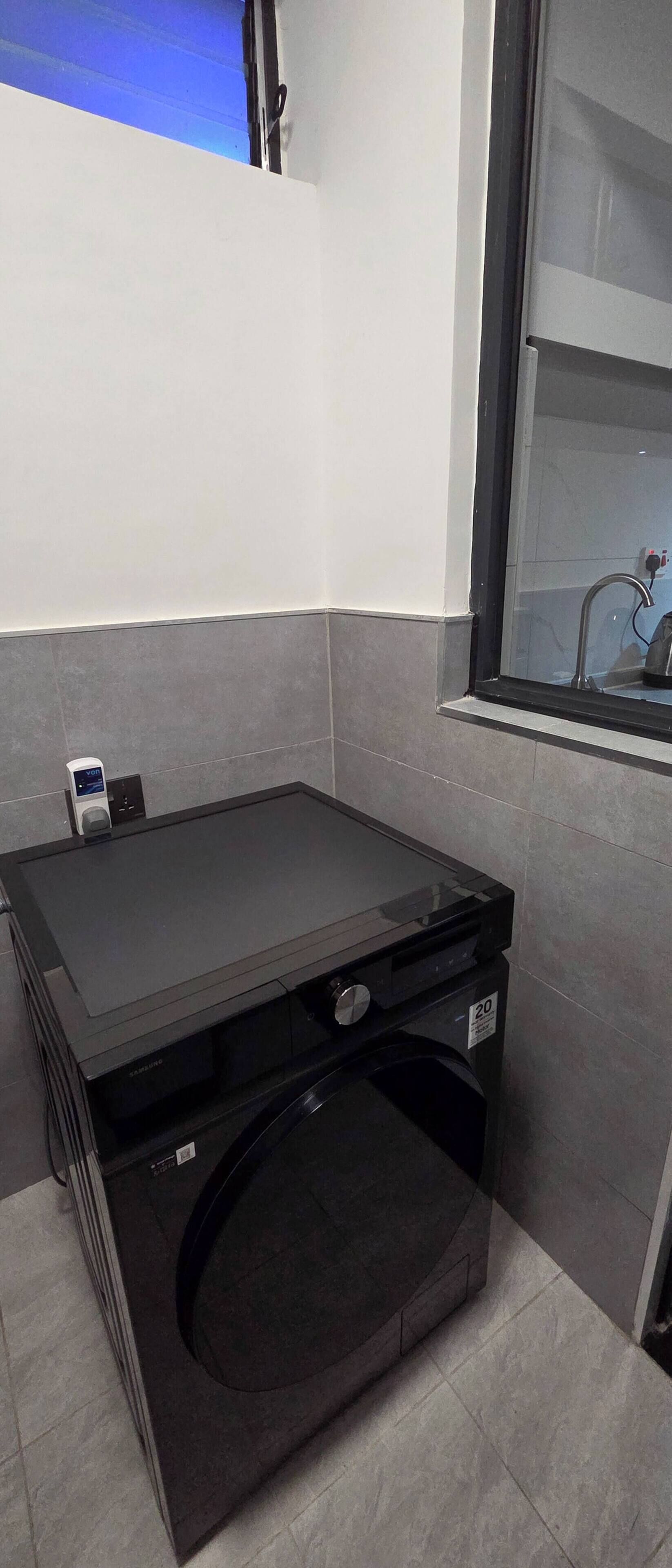 A compact, modern laundry room with a built-in washer and dryer, a small window, and a wall-mounted charging station.