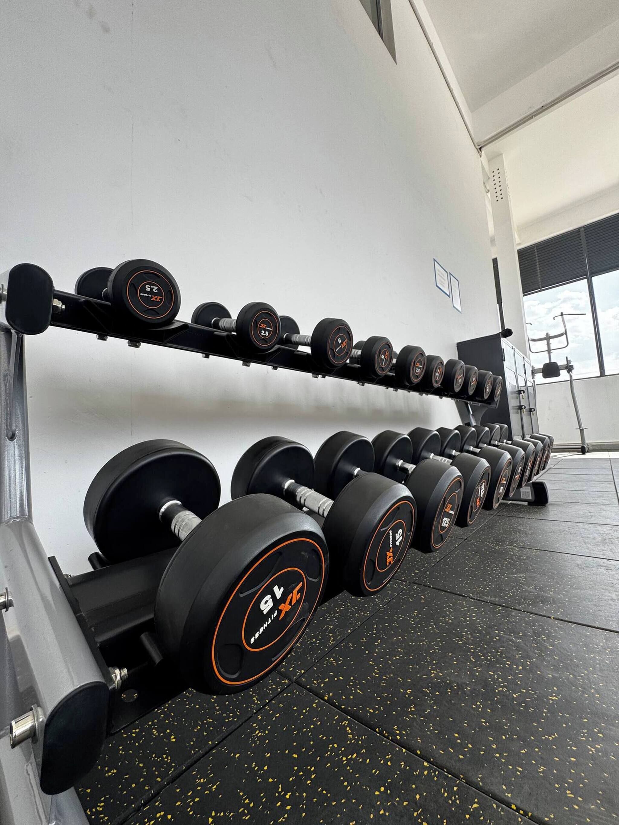 A gym with rows of dumbbells on racks and a weight bench.
