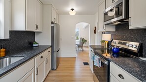 A modern kitchen with white cabinets, a stainless steel refrigerator, a microwave, and a gas stove.