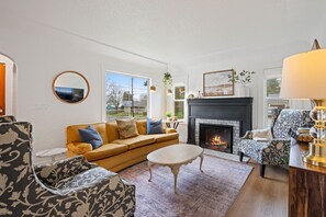 A living room with a sofa, armchairs, a fireplace, and a large window.