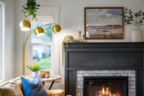 Een gezellige woonkamer met een open haard, een lijstwerk-landschap en een hangplant.