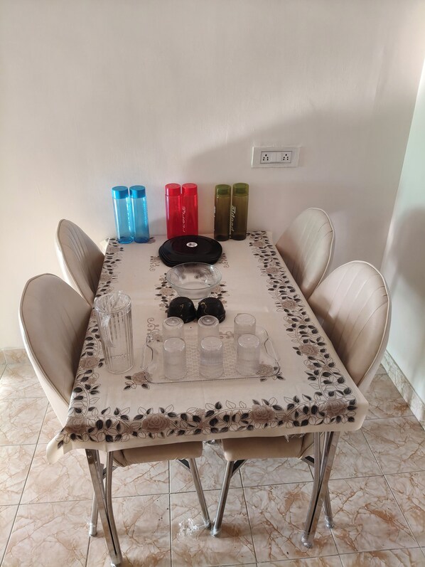 A dining table with a floral tablecloth, six clear glasses, two red and two green thermoses, and a black plate.