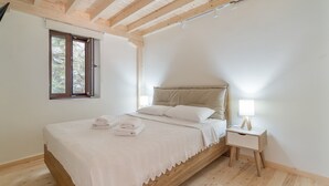 Ein Schlafzimmer mit einem hölzernen Bett, einem Nachttisch mit Lampe und einem Fenster mit Blick auf Bäume.