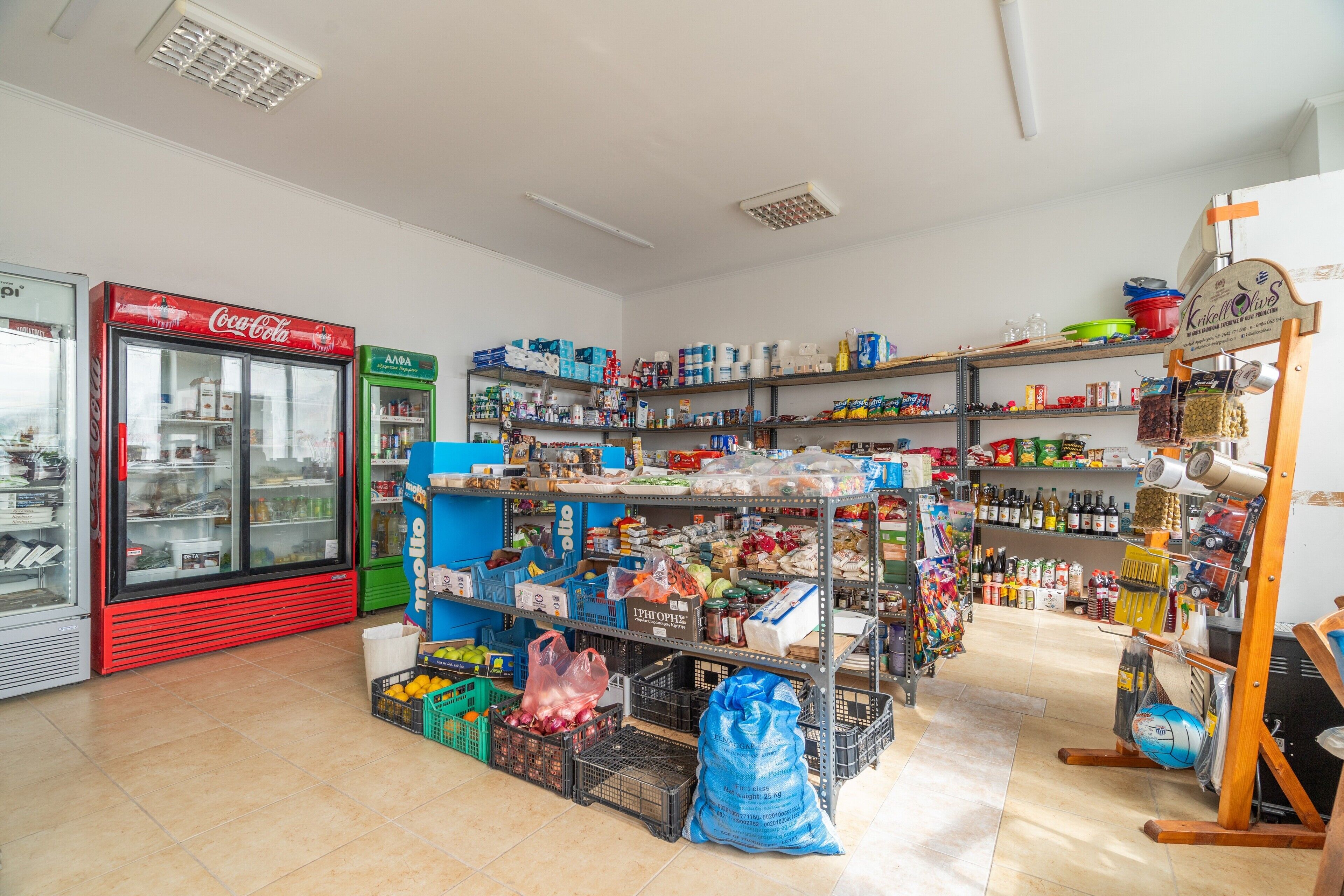 A grocery store with shelves stocked with various products, a Coca-Cola refrigerator, and a green refrigerator.