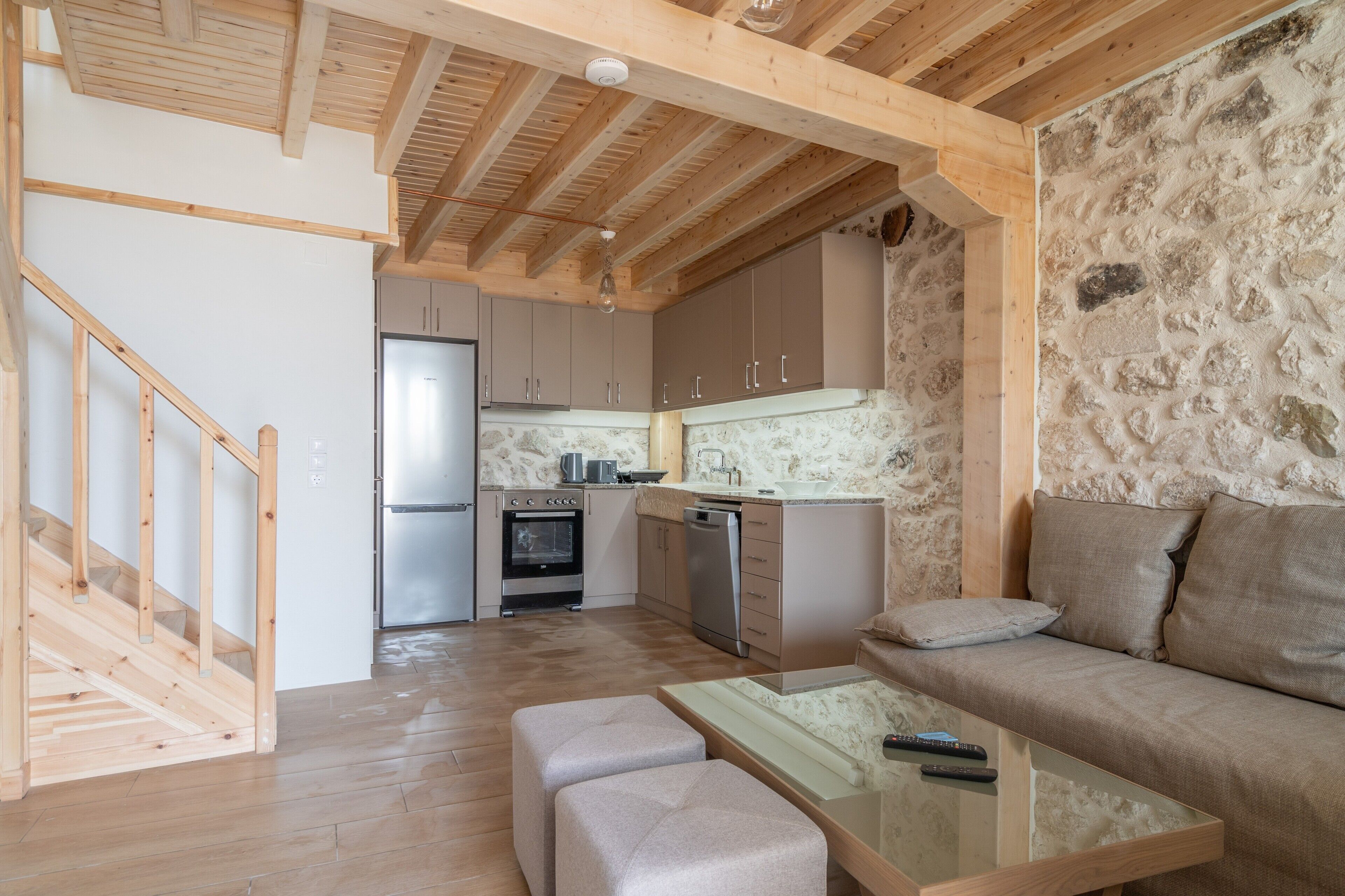 A modern kitchen with wooden beams, a stone wall, a sofa, and a glass table.