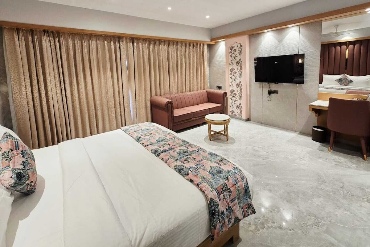 A hotel room with a bed, a sofa, a desk, a TV, and a large window with curtains.