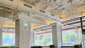 Een restaurant met hoge plafonds, luchtverwarming en een kroonluchter. Tafels en stoelen staan klaar voor het diner.