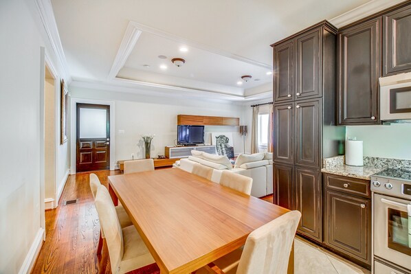 A modern kitchen with dark cabinets, a wooden dining table, and a built-in oven.