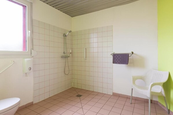 A small bathroom with a shower, a toilet, and a chair.