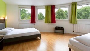 Habitación de hotel moderna con dos camas, un banco y ventanas amplias con cortinas rojas y verdes.