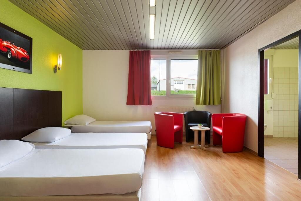 A hotel room with two beds, a small table, and red chairs.