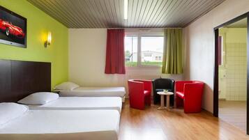 A hotel room with two beds, a small table, and red chairs.