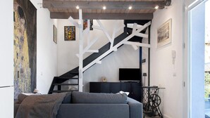 Uma sala de estar moderna com um sofá, uma escada, uma televisão e obras de arte nas paredes.