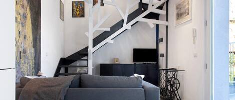 Een moderne woonkamer met een bank, een trap, een televisie en kunstwerken aan de muren.