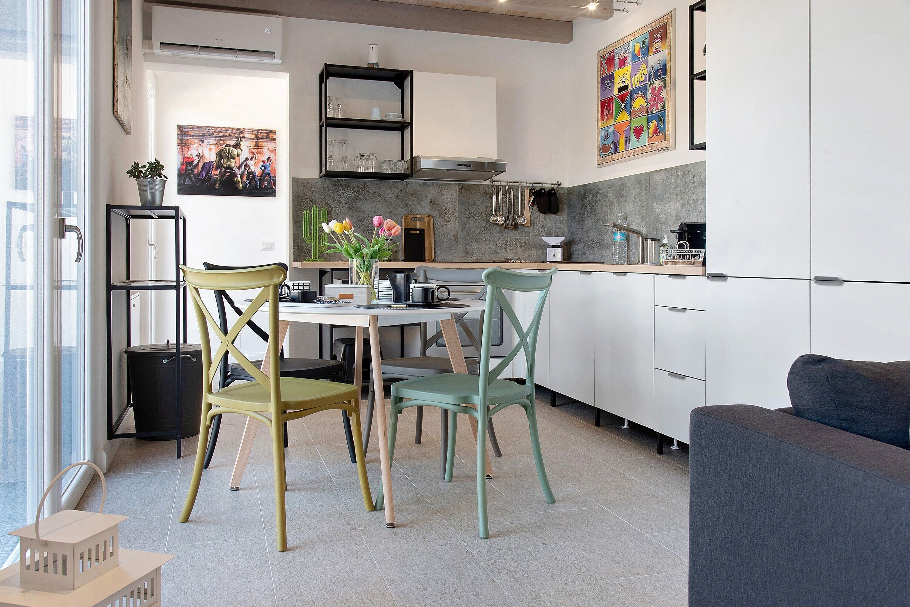 A modern kitchen with white cabinets, a dining table with chairs, and a grey sofa.